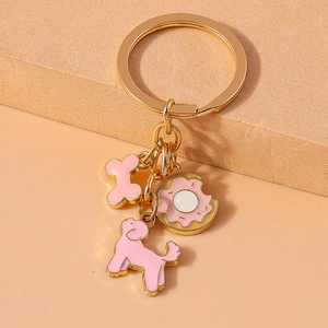 Detail of gold keychain with pink enamel poodle, cartoon bone and donut charms