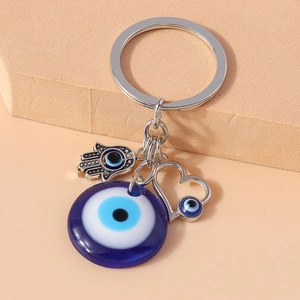 Evil Eye and Hamsa Hand keychain pendant with silver heart charm accessory on beige background
