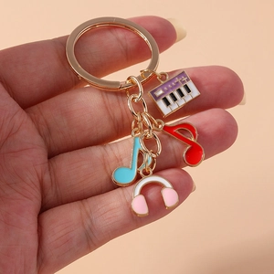 Porte-clés musical doré avec piano, notes colorées et charms casque rose tenus en main