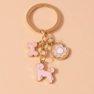 Close-up of golden keychain featuring pink bone, poodle dog, and donut enamel charms