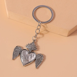 European vintage heart with wings keychain in antique silver finish on a beige surface