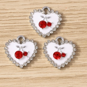Détail de pendentifs en cœur avec cadres argentés, strass et motifs cerises rouges