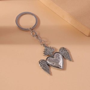 Vintage silver heart with wings keychain featuring a sacred heart flame design on beige