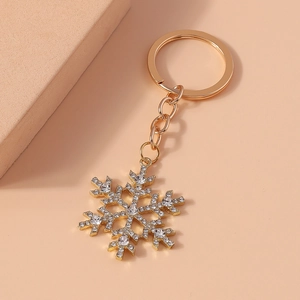 Golden snowflake keychain with sparkling white rhinestones on a warm neutral background