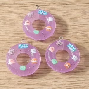 Drei lila transparente Harz-Donut-Anhänger mit Glitzer auf einer Holzoberfläche