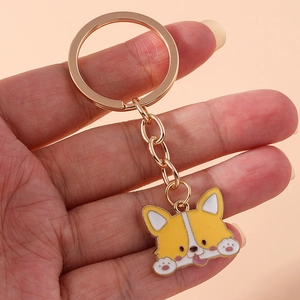 Detail of a cartoon Corgi keychain with gold metal chain held in hand for scale