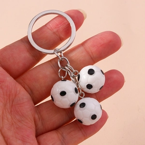 Detail showing hand holding silver key ring with three mini black and white soccer balls