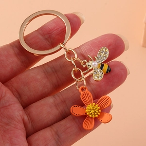 Golden keychain with orange flower and crystal bee pendant held against pink background