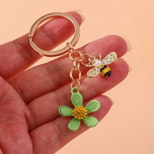 Golden keychain with rhinestone bee charm, pearl bead and green flower pendant in hand