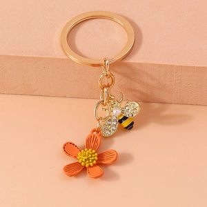 Detail of golden keychain featuring an orange flower charm and a crystal-set honey bee