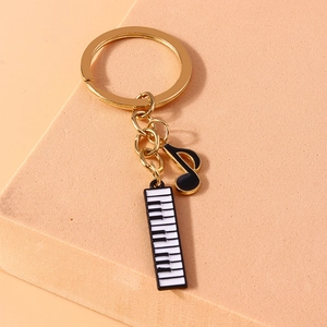 Golden musical keychain with enamel music note and piano keyboard pendants on a textured stand