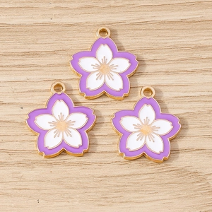 Detail of three purple cherry blossom alloy charms with gold edges on wood surface