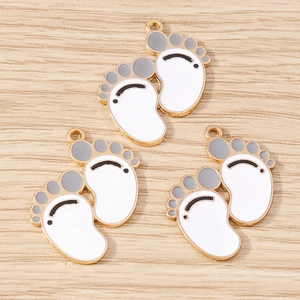 Close-up of three enamel baby footprint charms with gold trim for DIY jewelry making