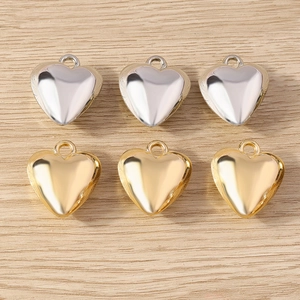 Polished gold and silver heart-shaped pendants for DIY jewelry on light wood surface