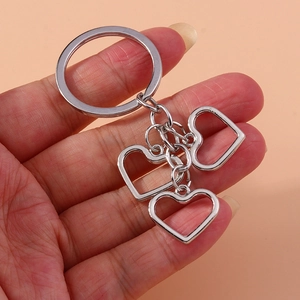 Minimalist silver metal keychain with three hollow heart pendants held in hand