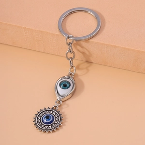 Evil eye keychain with silver sun and leaf pendants on a beige textured display