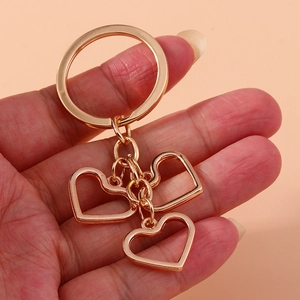 Handheld view of rose gold hollow heart keychain with three charms on simple pink background
