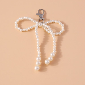 Romantic pearl beaded bow keychain accessory with silver metal clasp on warm background
