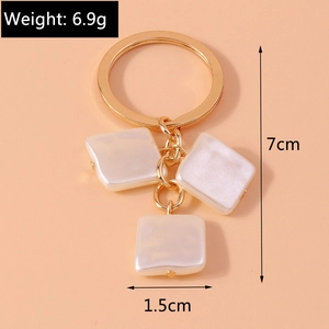 Detail showing white iridescent square pearl charms on a golden keychain link