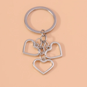 Macro detail of silver alloy heart keychain with hollow charms on pink background