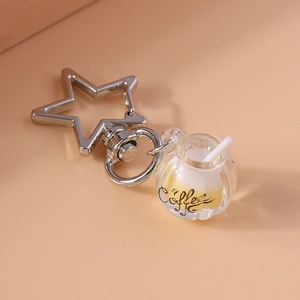 Detailed view of luminous coffee cup keychain with silver star clasp on pink background