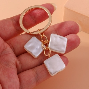 Detailed close-up of golden keychain with square white mother-of-pearl pendants