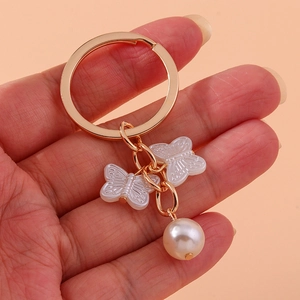 Elegant butterfly and pearl keychain with gold ring on soft pink background