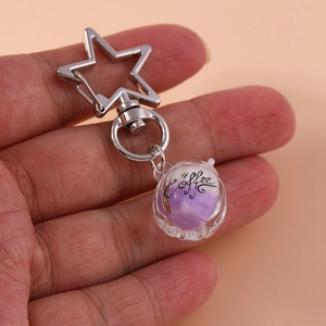Detailed close-up of a glowing coffee cup keychain with a silver star clasp and purple charm