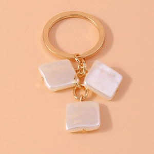 Detail of a gold-tone keyring with three square pendants featuring iridescent pearl finish