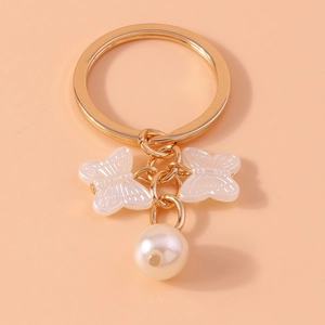 Detail of golden butterfly keychain with white resin charms and round pearl on orange background