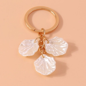 Detail of golden keychain with three pearlescent white flower petal pendants on pink background
