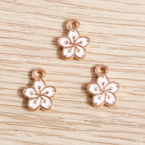 Drei Kirschblüten-Emaille-Anhänger in Roségold-Optik auf hellem Holzgrund