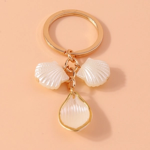 Detail of golden keychain with shell pendants and water drop pearl on beige background