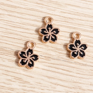 Drei Kirschblüten-Anhänger in Roségold mit schwarzer Emaille auf hellem Holzhintergrund