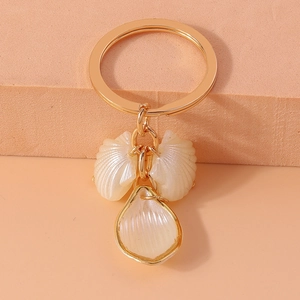 Detail of gold keychain with white shell pendants and iridescent petals on orange base