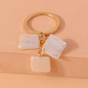 Detail view of golden keychain with three square pearl pendants on a display stand