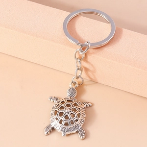 Vintage silver alloy sea turtle keychain with intricate hollow shell design on pink background