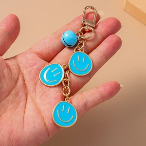 Dettaglio di ciondoli smiley in smalto blu e campanello dorato su un portachiavi moda