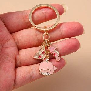 Goldener Schlüsselanhänger mit rosa Emaille-Wal und Seepferdchen vor rosa Hintergrund