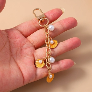 Detail of a gold lobster clasp keychain featuring orange enamel shells and white pearls