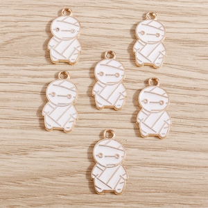 Détail macro de breloques momies en métal doré et émail blanc pour la création de bijoux