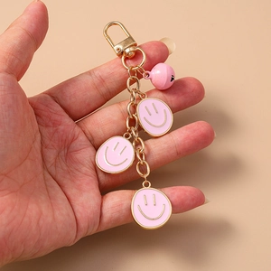 Dettaglio di ciondoli a forma di faccina rosa e campanellino su un portachiavi placcato oro