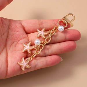 Cute pink starfish and pearl keychain charm with golden alloy chain in hand