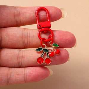 Cute cherry keychain with red enamel charms and a matching lobster clasp held in hand