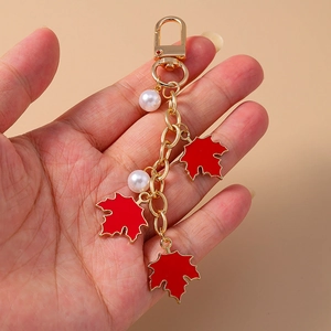 Detail of red maple leaf keychain with white pearls held by hand on beige backdrop