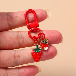 Handheld view of a cute strawberry keychain with red enamel charms and a metal clasp