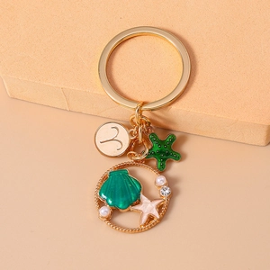 Detail of Aries gold keychain with green starfish and sea shell charms in a ring