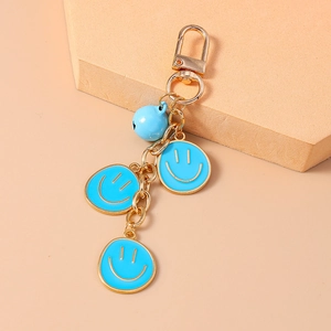 Dettaglio di ciondoli smiley in smalto blu e un campanellino dorato su un portachiavi