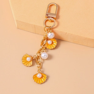 Close-up of golden keychain with yellow enamel sea shells and white pearl charms