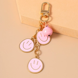 Dettaglio di ciondoli smiley in smalto rosa con catena dorata e portachiavi a campanella